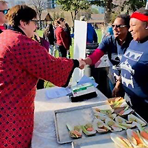 MnDOT commissioner margaret anderson kelliher reachs across a table with food to shake hands with two chefs.